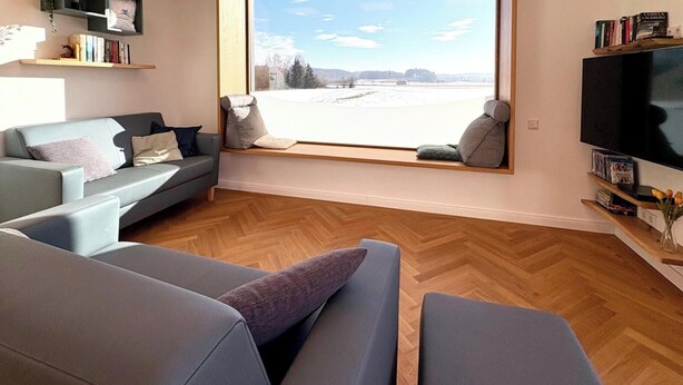 A modern living room with a sofa set, a television, and a large window offering a view of a snowy landscape. - Vacation apartment with 3 sep. Bedrooms and bathrooms (Nußdorf i. Chiemgau)