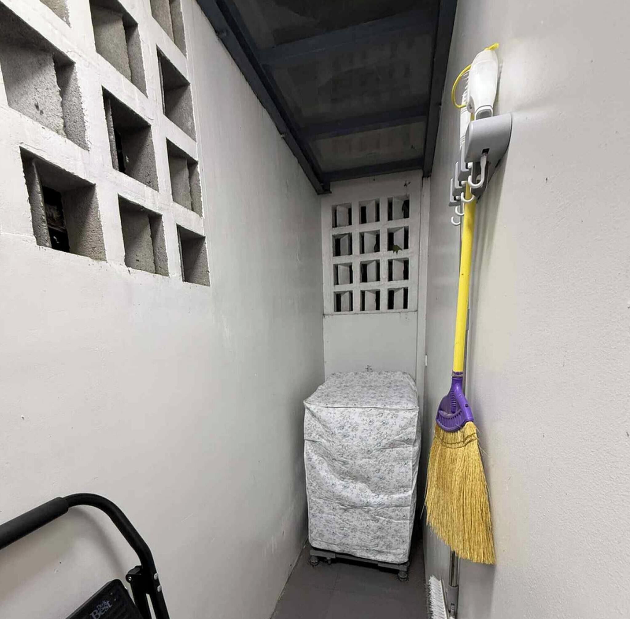 Ein schmaler Flur mit einem Fenster, einem abgedeckten Gegenstand und einem an der Wand angelehnten Besen.