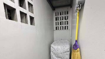 Ein schmaler Flur mit einem Fenster, einem abgedeckten Gegenstand und einem an der Wand angelehnten Besen.