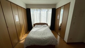 A bedroom with a single bed, wooden wardrobe, and a large window with curtains.