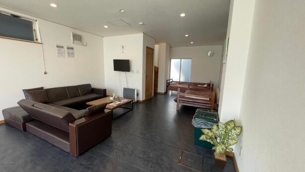 A modern living room with a dark brown sofa, a coffee table, and a TV mounted on the wall. There is a staircase leading to another level, and a potted plant on the floor.