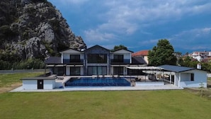 Une maison moderne à deux étages, dotée d’une grande piscine, avec une vue sur les montagnes et une pelouse bien entretenue.