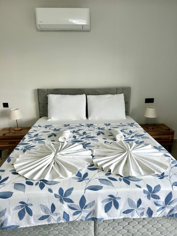 Una cama bien hecha con una colcha estampada de flores, dos almohadas y un arreglo decorativo de toallas.