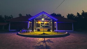A covered carport with a car parked inside, surrounded by a paved driveway and a small garden area. - Ammara Eco Stays (Chikkamagaluru)