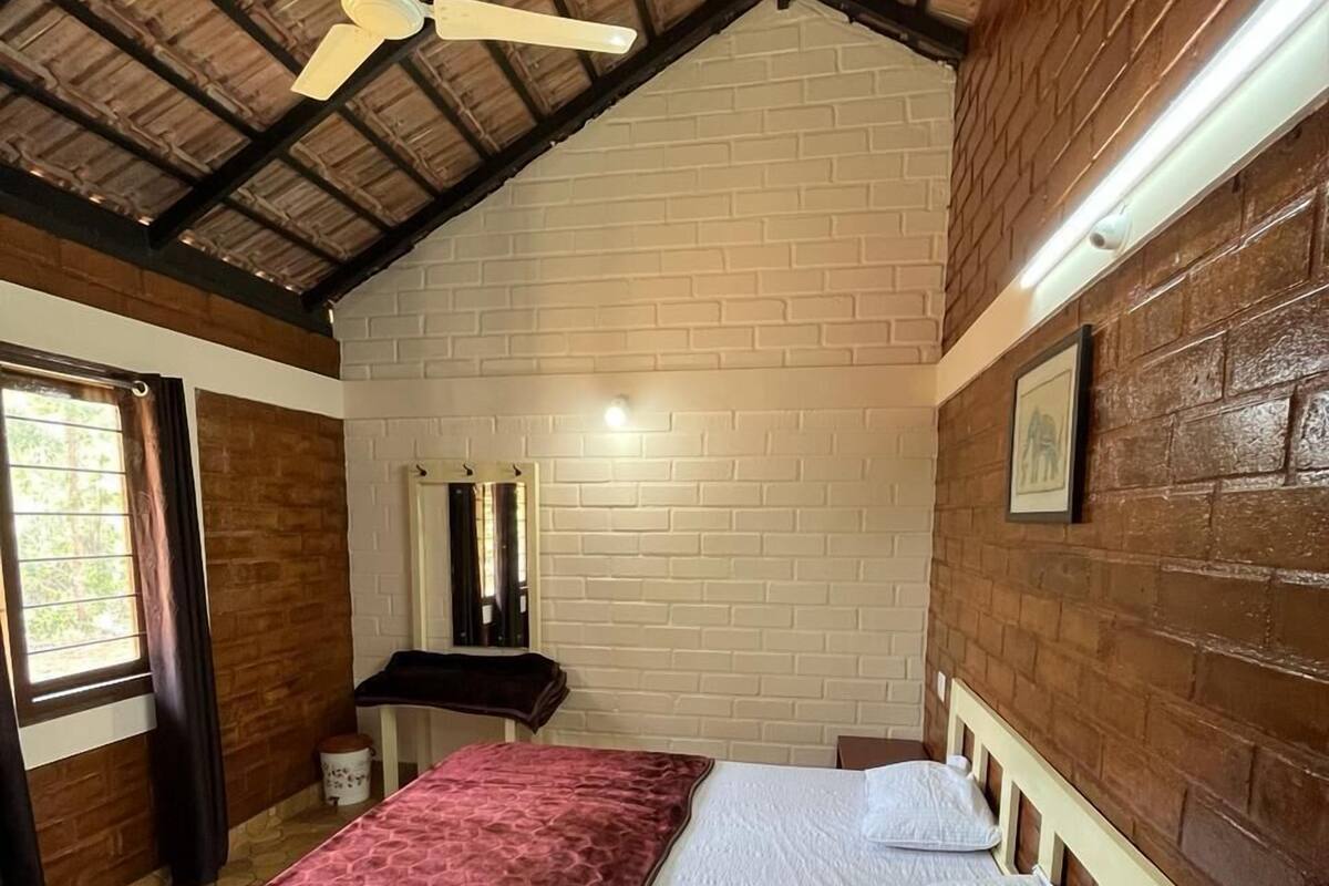 Una habitación con cama, ventilador de techo, pared de ladrillo y ventana.
