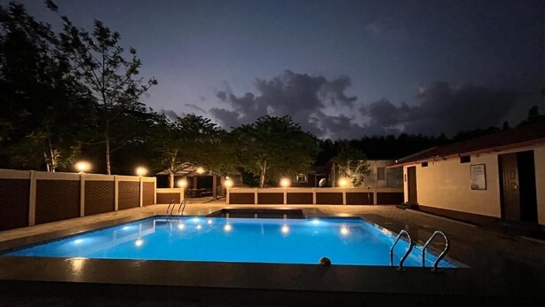 A rectangular swimming pool with a ladder on one side, surrounded by a low wall and a tiled deck. - Ammara Eco Stays (Chikkamagaluru)