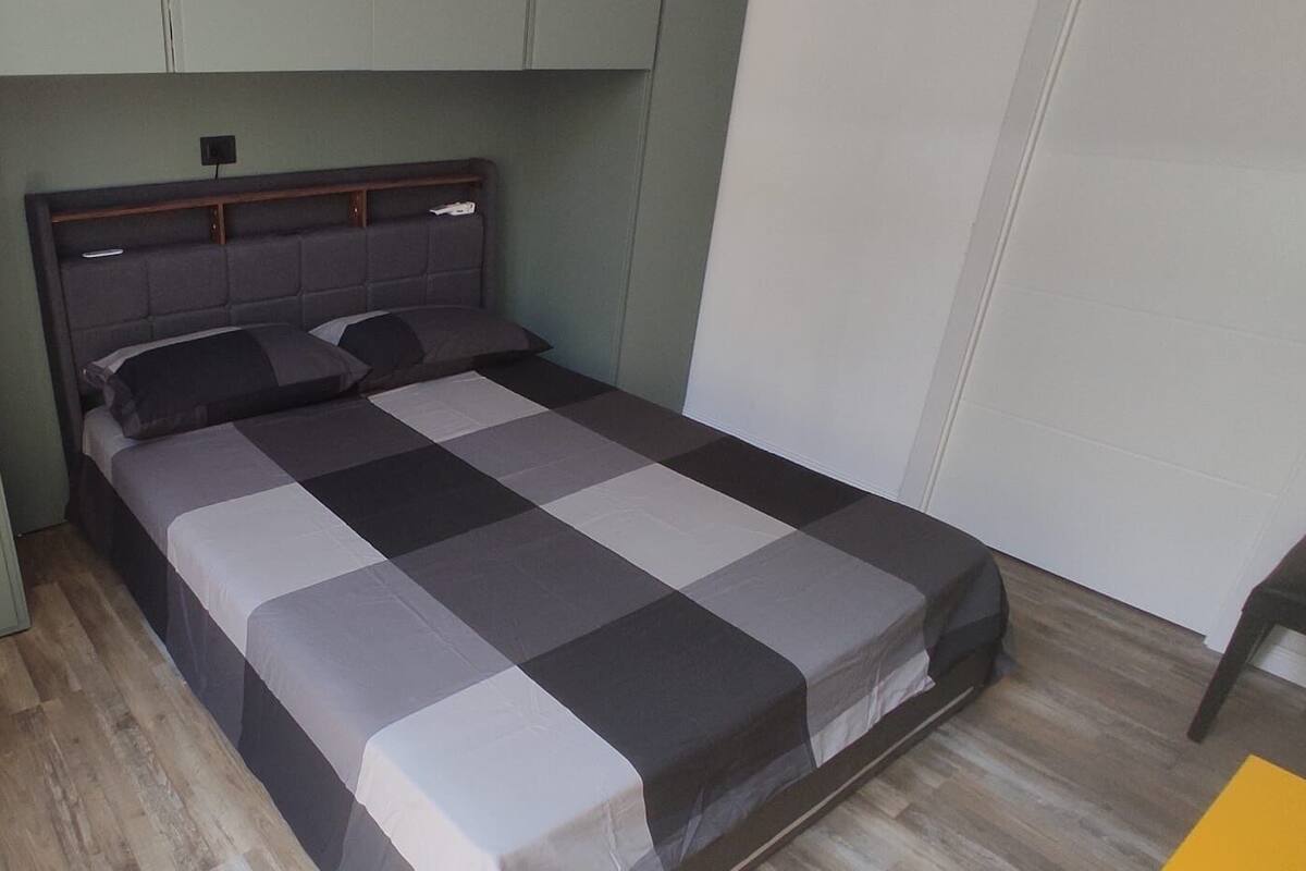 Un lit simple avec une couvre-lit à carreaux, dans une pièce aux murs verts et au plancher en bois.