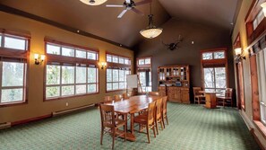 A spacious dining area with a large wooden table and chairs, surrounded by large windows with natural light.