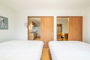Habitación de hotel con dos camas, un armario de madera, un cuadro de cebra y vistas a una cocina y zona de comedor.