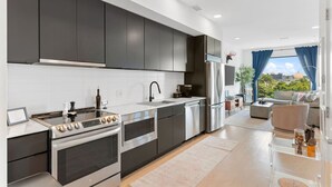 A modern kitchen with dark cabinets, stainless steel appliances, and a view to the living area.