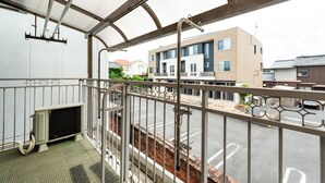 Un balcone con ringhiera in metallo, un tappetino verde e vista su una strada con edifici.