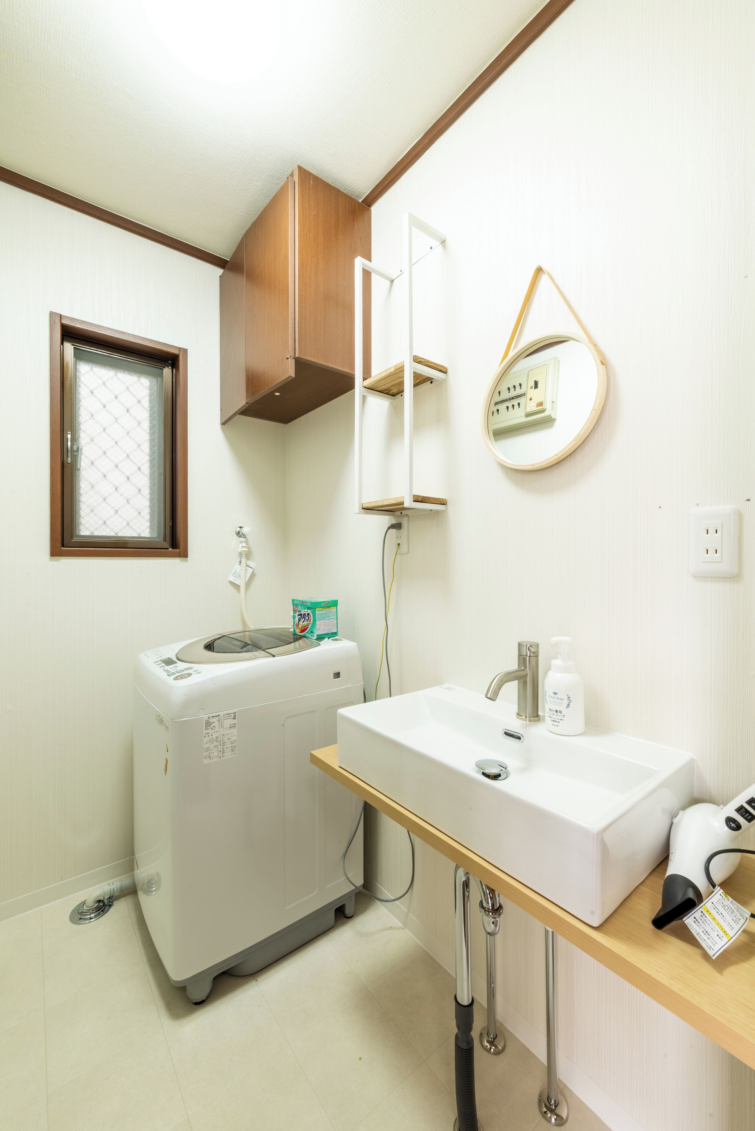 A compact bathroom with a white sink, a mirror, a hairdryer, and a washing machine.