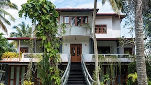 A two-story building with a staircase leading to the entrance, surrounded by lush greenery and palm trees. - Surf and Zen - Coworking and Coliving Habaraduwa (Habaraduwa)