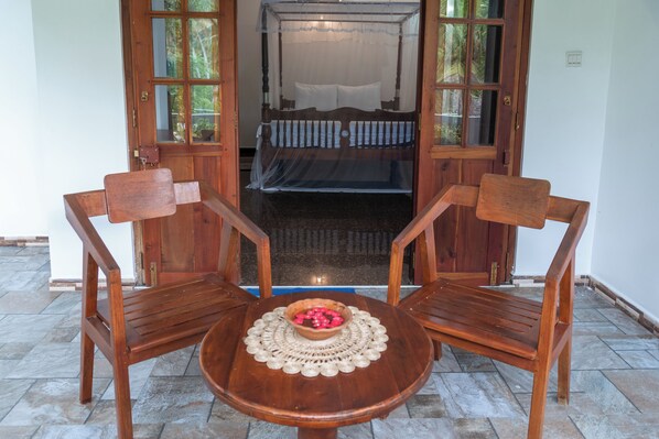 A wooden table with a bowl of fruit and two chairs in front of a bed with a canopy.
