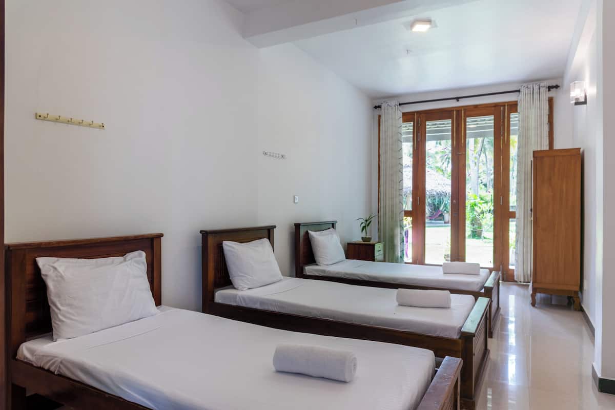 Habitación de hotel con tres camas individuales, un armario de madera y un ventanal con cortinas.