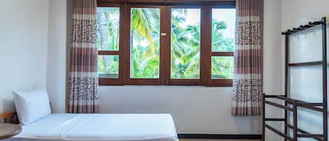 Una cama individual en una habitación con ventana, cortinas y cabecera de madera.