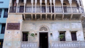 A historic building with a sign reading "Vivaia museum hotel." It features ornate balconies, a central entrance with a decorative arch, and two potted plants. - Vivaana  Museum Hotel (Nawalgarh)