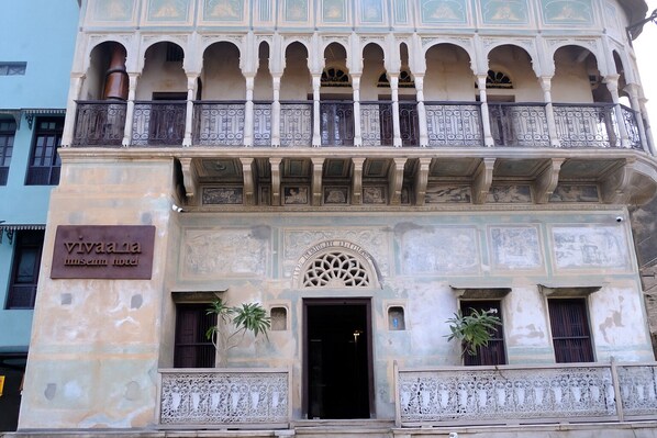 Un edificio histórico con un cartel que dice "Vivaia museum hotel". Cuenta con balcones ornamentados, una entrada central con un arco decorativo y dos macetas.