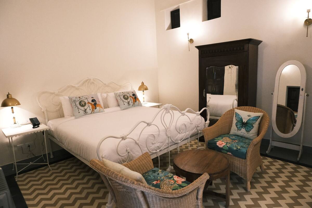 A bedroom with a bed, two chairs, a dresser, and a mirror.