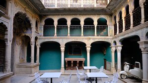 A courtyard with ornate arches, a central fireplace, and white tables and chairs. - Vivaana  Museum Hotel (Nawalgarh)