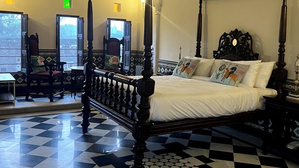 A four-poster bed with a checkered floor, a window with a view, and a wall-mounted air conditioner. - Vivaana  Museum Hotel (Nawalgarh)