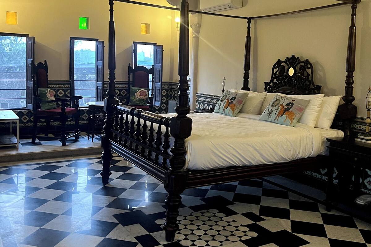 A four-poster bed with a checkered floor, a window with a view, and a wall-mounted air conditioner.