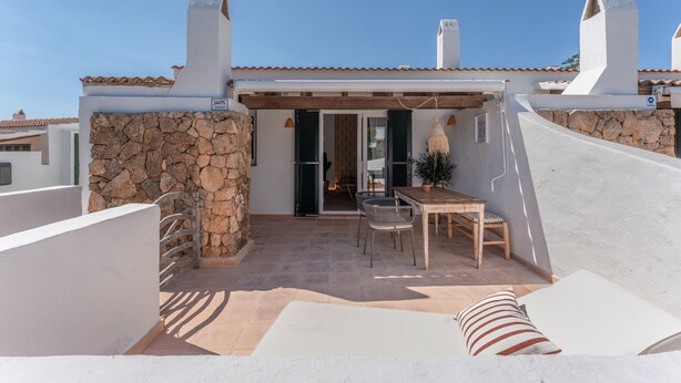 A patio with a table and chairs, a stone wall, and a view of the interior. - Holiday Home 'Villa 19 Estrellas' with Pool, Garden and Private Terrace (Cap d'Artrutx)