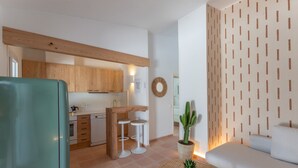 A modern kitchen with wooden cabinets, a dining area with stools, a living room with a sofa, and a potted cactus. - Holiday Home 'Villa 19 Estrellas' with Pool, Garden and Private Terrace (Cap d'Artrutx)
