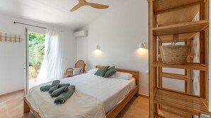 A bedroom with a bed, a ceiling fan, a wooden shelf with a basket, a chair, and a door leading to a balcony. - Holiday Home 'Villa 19 Estrellas' with Pool, Garden and Private Terrace (Cap d'Artrutx)