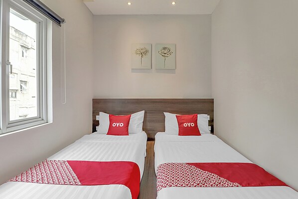 Habitación de hotel con dos camas, cada una con ropa de cama roja y blanca, y una ventana que ofrece vistas a la calle.