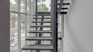 A metal staircase with a metal handrail, leading to an outdoor area with a view of a street and trees. - Capital O 94727 Regia Cihampelas Ciwalk (Bandung)