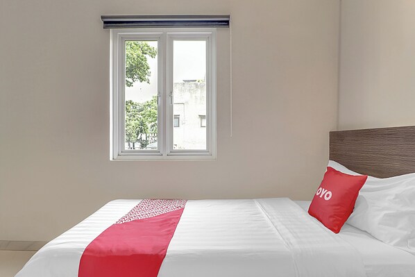 A neatly made bed with a red and white bedspread, a wooden headboard, and a window with a view of the outside.