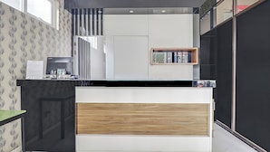 A modern reception desk with a wooden panel, a black countertop, and a white wall with a patterned wallpaper. - Capital O 94727 Regia Cihampelas Ciwalk (Bandung)