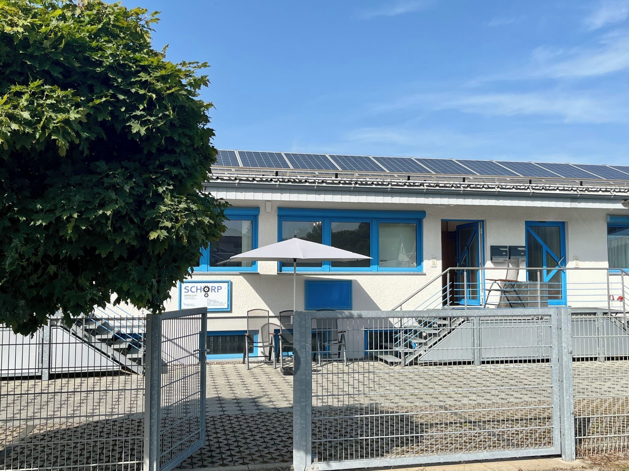 Un edificio con paneles solares, puertas azules y un letrero que dice 'SCHORP'.