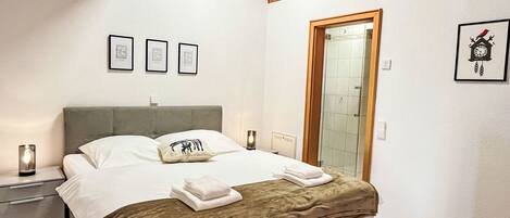 Un dormitorio con cama, mesitas de noche, un zapatero, una viga de techo de madera, una puerta y cuadros en la pared.