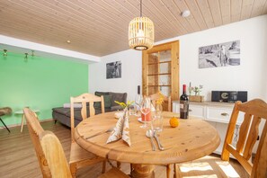 A dining area with a round wooden table, chairs, a hanging light fixture, and a green wall. - Apartment 'Harmonie' with Shared Garden and Wi-Fi (Oberreute)