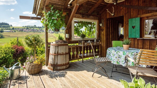 Una terraza de madera con una mesa y sillas, una planta colgante y vistas a un pueblo.