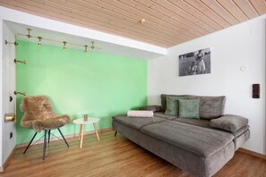 A room with a green wall, a grey sofa, a furry chair, a small round table, and a wooden ceiling. - Apartment 'Harmonie' with Shared Garden and Wi-Fi (Oberreute)