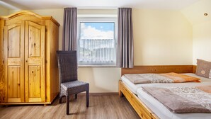 Un dormitorio con un armario de madera, una silla, una cama con ropa de cama estampada y una ventana con cortinas.