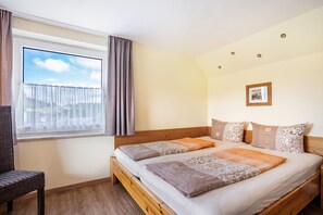 A bedroom with a wooden bed, a window with curtains, a chair, and a framed picture on the wall. - Apartment 'Harmonie' with Shared Garden and Wi-Fi (Oberreute)