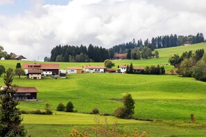 Un paysage rural avec des maisons à flanc de colline, entourées de champs verdoyants et d’arbres.