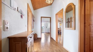 Een hal met houten vloer, een houten kast, een wandlamp en een spiegel.