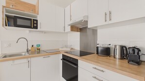 Une cuisine moderne avec des meubles blancs, un évier en acier inoxydable, un four à micro-ondes, un grille-pain et une bouilloire.