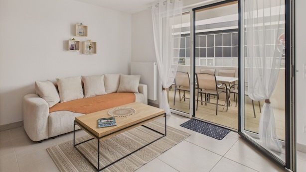 Un salon moderne avec un canapé, une table basse et un coin repas visible à travers une porte vitrée.