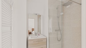 Une salle de bain moderne avec une douche à parois de verre, un lavabo blanc avec un miroir et des tiroirs en bois.
