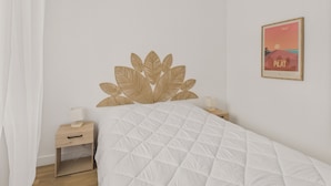 Une chambre avec un lit blanc, une tête de lit en bois ornée de motifs de feuilles, une petite table de chevet avec une lampe et un tableau encadré accroché au mur.