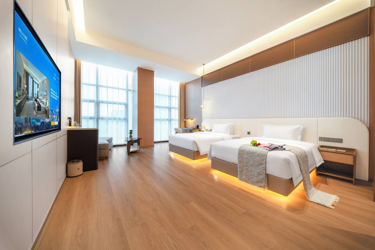 Une chambre d’hôtel moderne avec deux lits, un bureau, une télévision et de grandes fenêtres.