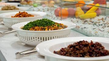 A buffet with various dishes, including a bowl of green vegetables and a bowl of red sauce.