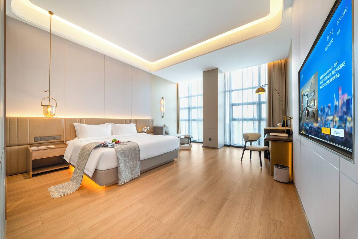 Une chambre d’hôtel moderne avec un grand lit, des tables de chevet, un bureau et une grande fenêtre.
