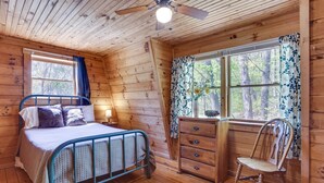 A wooden cabin bedroom with a bed, a desk, and a chair.